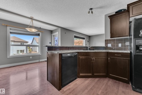 Kitchen featuring dark wood-finish cabinetry, granite-style countertops, and a tile backsplash - 6116 11 Avenue, Edmonton, AB 