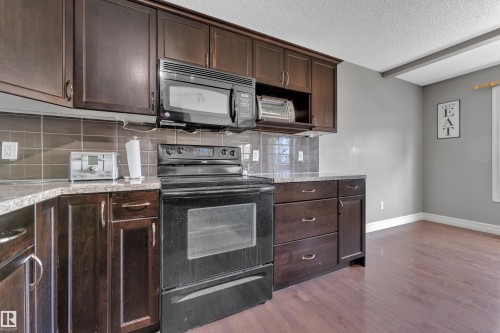 Kitchen featuring dark wood cabinetry, a black range with an overhead microwave, tile backsplash, and light-toned countertops - 6116 11 Avenue, Edmonton, AB 