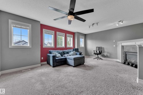 Spacious living area featuring carpet flooring, a ceiling fan, multiple windows with white trim, a decorative fireplace with a mantel, and track lighting - 6116 11 Avenue, Edmonton, AB 