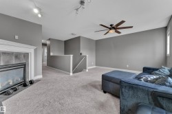 Carpeted living space featuring a fireplace with a tile surround and white mantel, a ceiling fan with light fixture, and track lighting - 