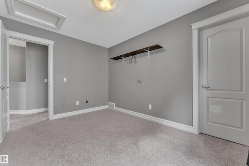 Neutral-toned room featuring a light gray carpet, matching wall paint, and white trim - 6116 11 Avenue, Edmonton, AB 