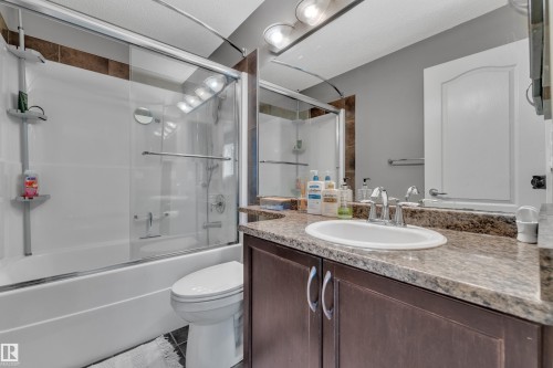 Bathroom featuring a white tub-shower combination with glass enclosure, single vanity with a granite-style countertop, and dark wood-finish cabinetry - 6116 11 Avenue, Edmonton, AB 