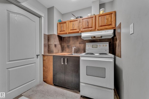 Compact kitchen area featuring a white electric range, integrated range hood, and a stainless steel sink with a chrome faucet - 6116 11 Avenue, Edmonton, AB 