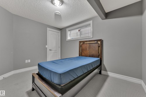Bedroom featuring light gray carpet, neutral gray walls, white trim, a white interior door, and a horizontal window with blinds - 6116 11 Avenue, Edmonton, AB 