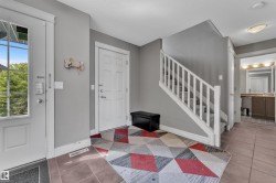 Entrance foyer featuring ceramic tile flooring, a staircase with carpeted treads and white wood railing, a partial light gray painted wall, and a powder room with a vanity and mirror - 