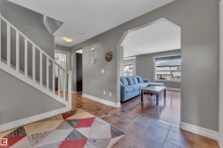 Foyer featuring a staircase with white balusters, ceramic tile flooring, and an arched entryway opening to a living area with wood-finish flooring and large windows - 