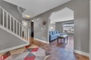 Foyer featuring a staircase with white balusters, ceramic tile flooring, and an arched entryway opening to a living area with wood-finish flooring and large windows - 6116 11 Avenue, Edmonton, AB 