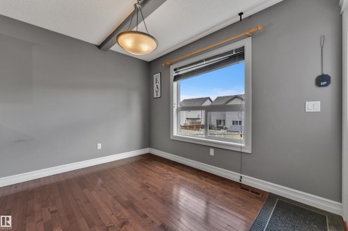 Spacious room featuring wood-finish flooring, ample natural light from a large window, a ceiling-mounted light fixture, and neutral gray wall tones - 6116 11 Avenue, Edmonton, AB 