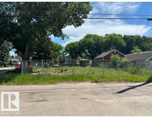 Vacant lot featuring a chain-link perimeter fence, mature trees, and undeveloped ground - 12072 95 Street, Edmonton, AB 