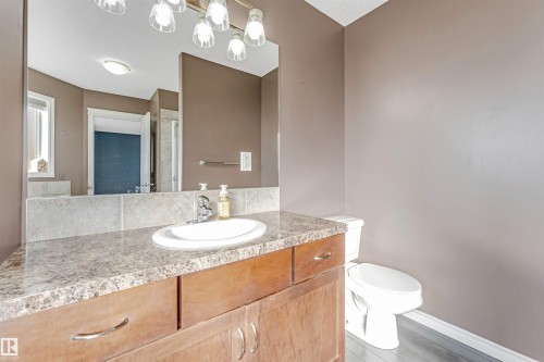 Bathroom vanity with a white oval sink, speckled countertop, and wood-finish cabinetry - 5928 12 Avenue, Edmonton, AB 