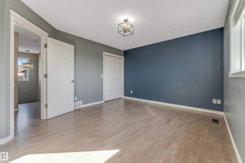 Spacious room featuring light wood-finish flooring, a contemporary geometric ceiling fixture, and a window with white trim - 5928 12 Avenue, Edmonton, AB 