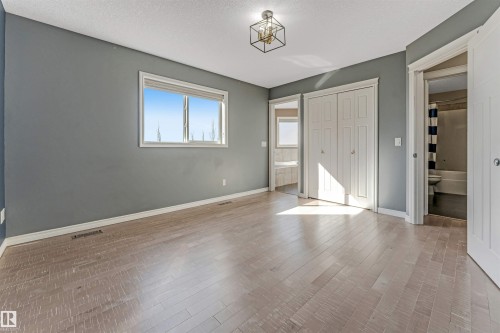 Spacious room featuring light wood-finish flooring, a window with white trim, and a contemporary ceiling light fixture - 5928 12 Avenue, Edmonton, AB 