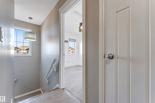 Stairwell featuring wood-finish flooring, a window with grid patterns, a decorative pendant light, and a white handrail - 5928 12 Avenue, Edmonton, AB 