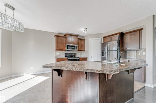 Kitchen featuring a large central island with an integrated sink, dark wood cabinetry, stainless steel appliances, and a tiled backsplash - 5928 12 Avenue, Edmonton, AB 