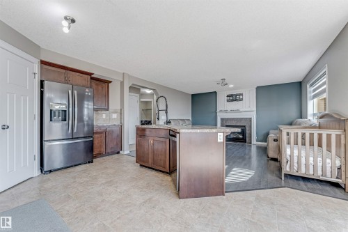 Open-concept living space featuring a kitchen island with stone-finish countertops, stainless steel appliances, and wood cabinetry - 5928 12 Avenue, Edmonton, AB 