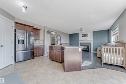 Open-concept living space featuring a kitchen island with stone-finish countertops, stainless steel appliances, and wood cabinetry - 