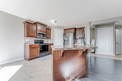 Kitchen featuring dark wood cabinetry, stainless steel appliances, stone-finish countertops, and a central island with an integrated sink - 5928 12 Avenue, Edmonton, AB 