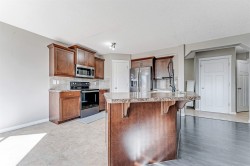 Kitchen featuring dark wood cabinetry, stainless steel appliances, stone-finish countertops, and a central island with an integrated sink - 