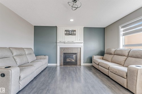 Living area featuring a central fireplace with a tile surround and white mantelpiece, recessed lighting, wood-finish flooring, and a large window with roller blinds - 5928 12 Avenue, Edmonton, AB 