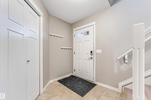 Entryway featuring neutral wall tones, ceramic tile flooring, a paneled front door with decorative glass inserts, and a built-in closet with bi-fold doors - 5928 12 Avenue, Edmonton, AB 