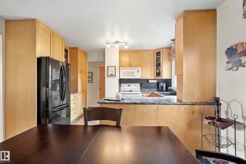 Kitchen featuring light wood-finish cabinetry, black appliances, track lighting, and a dark stone countertop - 3208 70 Street, Edmonton, AB 