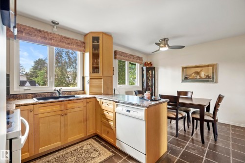 Kitchen featuring light wood cabinetry, stone-finish countertops, a corner display cabinet with glass doors, and a built-in dishwasher - 3208 70 Street, Edmonton, AB 