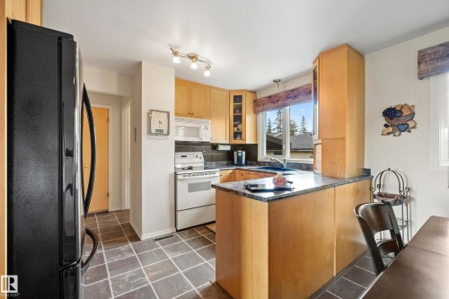 Kitchen featuring stone-finish floor tiles, light wood cabinetry, white appliances, and a black refrigerator - 3208 70 Street, Edmonton, AB 