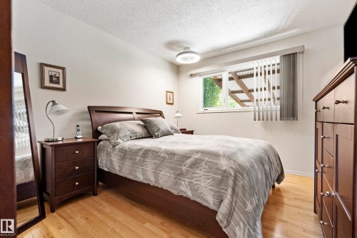 Bedroom featuring light wood-finish flooring, a contemporary ceiling light fixture, a window with vertical blinds, and a textured white ceiling - 3208 70 Street, Edmonton, AB 