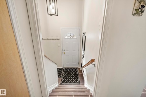 Entryway featuring a white paneled door with an arched glass insert, dark tiled flooring, a wooden handrail, and a contemporary black metal pendant light fixture - 3208 70 Street, Edmonton, AB 