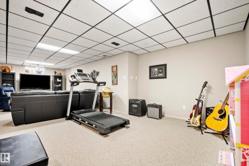 Spacious recreational room featuring light-colored carpeting, a grid drop ceiling with integrated lighting, and neutral wall tones - 3208 70 Street, Edmonton, AB 