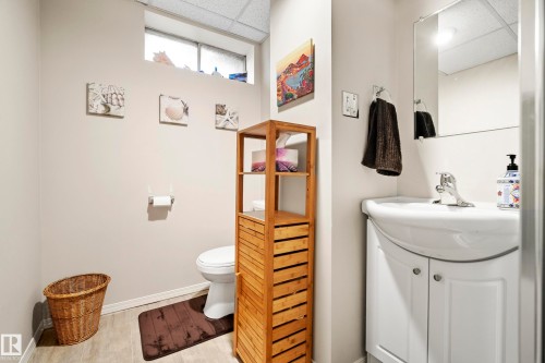 Compact bathroom featuring a white ceramic toilet, a vanity with a white basin and cabinet storage, a mirrored medicine cabinet, and wood-finish flooring - 3208 70 Street, Edmonton, AB 