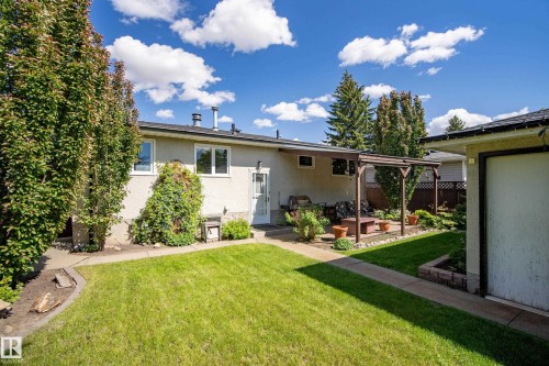 Expansive backyard featuring a manicured lawn, paved walkway, and a covered patio area - 3208 70 Street, Edmonton, AB 