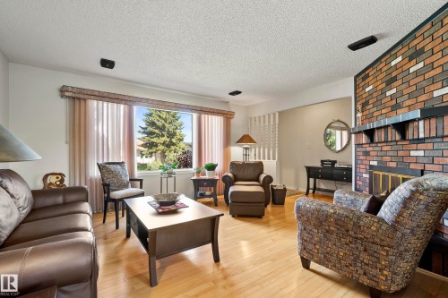 Living area with a brick fireplace, blonde wood-finish flooring, and a large window - 3208 70 Street, Edmonton, AB 