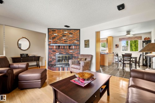 Living area featuring hardwood-finish flooring, a multi-tone brick fireplace with hearth, and an open entryway to the dining area - 3208 70 Street, Edmonton, AB 