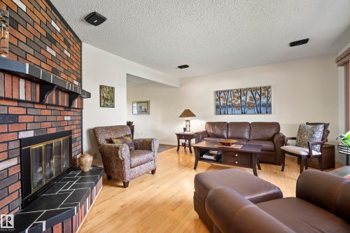 Living area featuring a brick fireplace with a black tile hearth and mantel, light wood-finish flooring, and white walls - 3208 70 Street, Edmonton, AB 