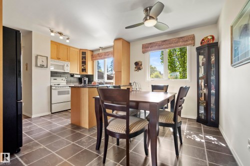 Kitchen and dining area featuring dark tile flooring, light wood-finish cabinetry, a peninsula countertop, and a ceiling fan with integrated lighting - 3208 70 Street, Edmonton, AB 