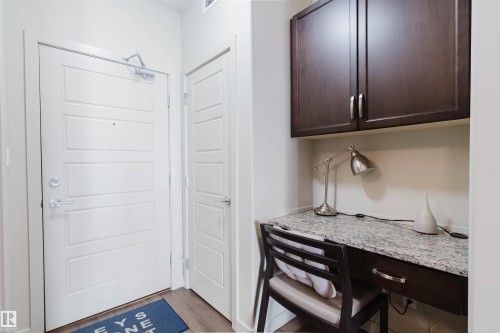 Dedicated work area featuring a speckled countertop, rich wood-finish cabinetry, and wood-finish flooring - 217 508 Griesbach Parade, Edmonton, AB 
