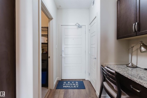 Entryway featuring wood-finish flooring, a contemporary paneled door, and an integrated desk area - 217 508 Griesbach Parade, Edmonton, AB 
