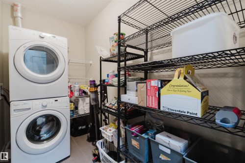 Dedicated laundry area featuring a stacked washer and dryer unit, wire shelving, and neutral tone walls - 217 508 Griesbach Parade, Edmonton, AB 