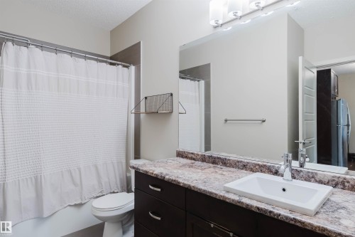 Bathroom featuring a vanity with a rectangular basin sink, mottled countertop, and dark wood-finish cabinetry - 217 508 Griesbach Parade, Edmonton, AB 