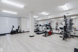 Spacious fitness center featuring light wood-finish flooring, full-wall mirrors, abundant overhead lighting, and white window blinds - 