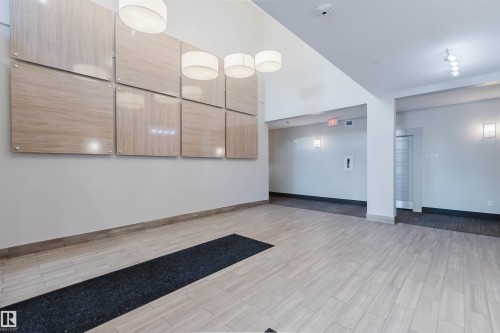 Spacious entry area featuring light-toned wood-finish flooring, a wall display of large square panels, and contemporary ceiling light fixtures - 217 508 Griesbach Parade, Edmonton, AB 