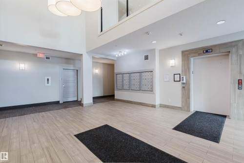 Spacious lobby featuring wood-finish flooring, a two-story ceiling, multiple wall sconces, a contemporary chandelier, and an elevator with a wood-look surround - 217 508 Griesbach Parade, Edmonton, AB 