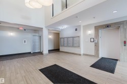 Spacious lobby featuring wood-finish flooring, a two-story ceiling, multiple wall sconces, a contemporary chandelier, and an elevator with a wood-look surround - 