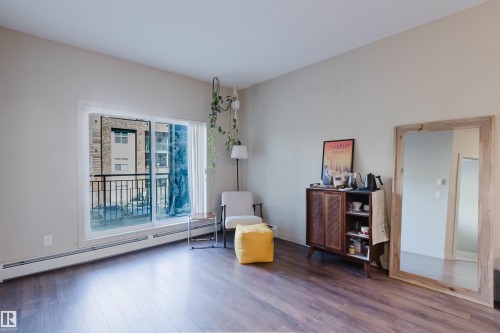 Spacious interior featuring wood-finish flooring, light neutral wall paint, and a large sliding glass door opening to a private balcony with black metal railings - 217 508 Griesbach Parade, Edmonton, AB 