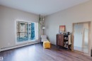 Spacious interior featuring wood-finish flooring, light neutral wall paint, and a large sliding glass door opening to a private balcony with black metal railings - 217 508 Griesbach Parade, Edmonton, AB 
