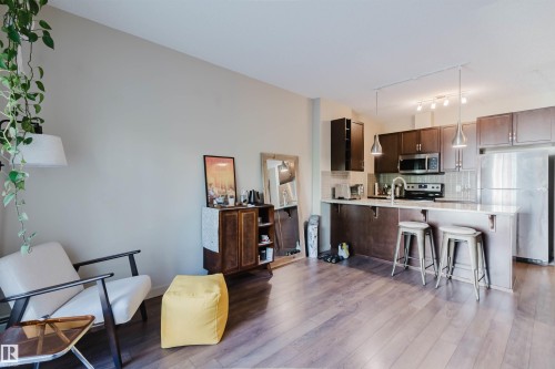 Open-concept kitchen featuring dark wood cabinetry, stainless steel appliances, a tile backsplash, and a breakfast bar with pendant lighting - 217 508 Griesbach Parade, Edmonton, AB 