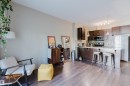 Open-concept kitchen featuring dark wood cabinetry, stainless steel appliances, a tile backsplash, and a breakfast bar with pendant lighting - 217 508 Griesbach Parade, Edmonton, AB 