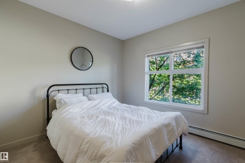 Carpeted room with a large window, neutral wall paint, white trim, and baseboard heating - 217 508 Griesbach Parade, Edmonton, AB 