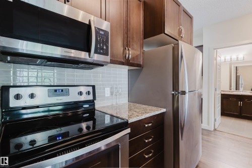 Contemporary kitchen with stainless steel appliances, dark wood cabinetry, light speckled countertops, and a subway tile backsplash - 217 508 Griesbach Parade, Edmonton, AB 